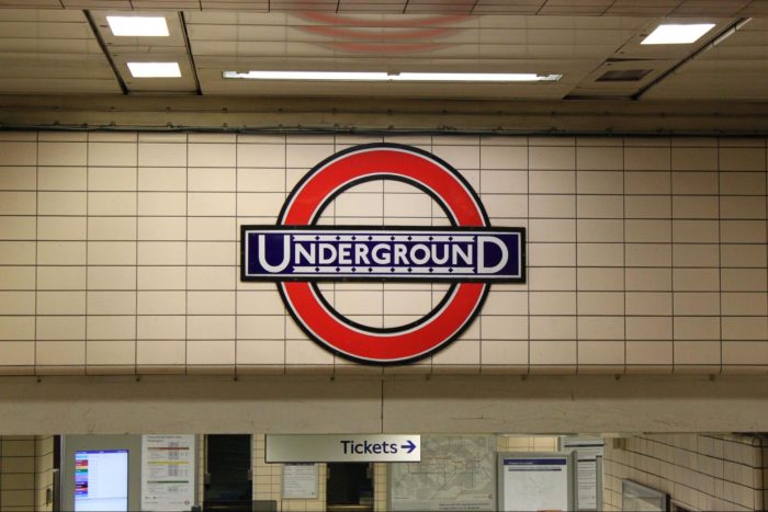 Entrance to a tube station with a clear overhead sign displaying the Underground and white metro tiles.